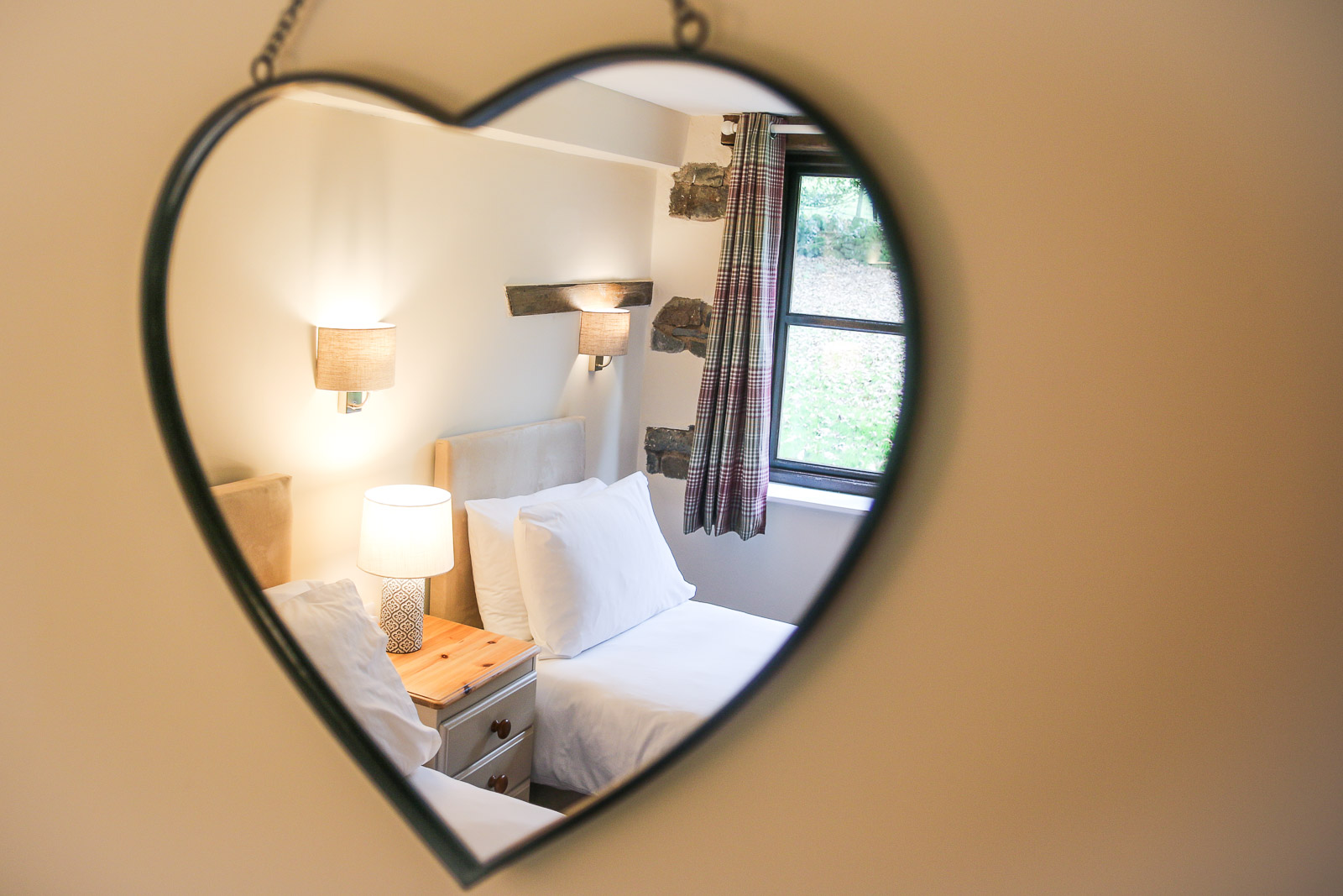 A heart-shaped mirror with a bedroom in the reflection.